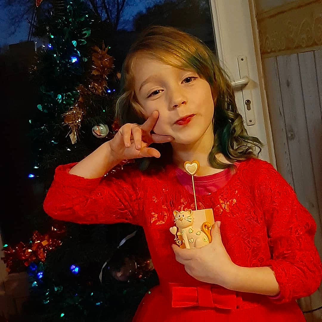 Lola a rejoint le concours — aidez-le/la à gagner de superbes lots ! arm, christmas, christmas_decoration, christmas_ornament, christmas_tree, door, dress, event, eyelash, fashion_design, fun, happy, head, holiday_ornament, human_body, long_hair, ornament, person, sleeve, standing