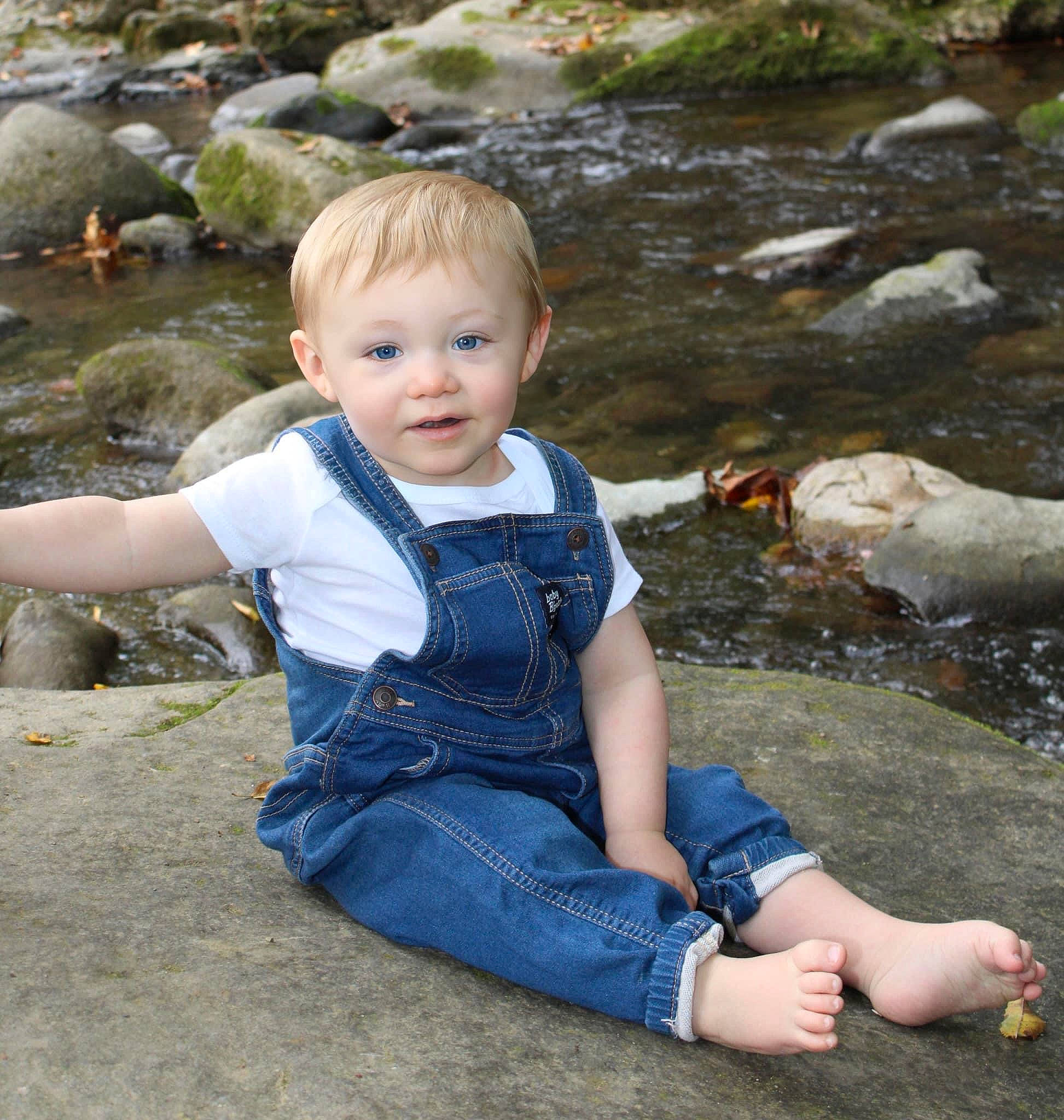 Emmet is registered to the contest to win money with this photo: baby_toddler_clothing, bank, child, fun, grass, happy, leaf, leisure, mammal, people_in_nature, person, plant, rock, sitting, stream, summer, toddler, tree, vertebrate, water