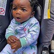 Kolby joined the competition — help win amazing prizes! baby, child, car_seat, dinosaur_pajamas, curly_hair, bantu_knots, hands, expression, wide_eyes, infant, seatbelt_warning_labels, clothing, portrait, cute, indoors, seat, person, young_child, sitting, closeup