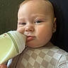 baby, infant, child, bottle, feeding, formula, face, portrait, close_up, indoors, sitting, lying_down, onesie, checkered_clothing, blanket, happy, calm, eyes, tongue, photography