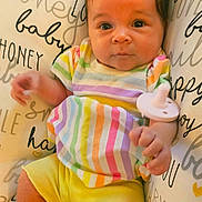 Luna joined the competition — help win amazing prizes! baby, infant, child, colorful_clothing, striped_shirt, yellow_shorts, pacifier, pillow, text_print, script_text, cute, curious_eyes, soft_lighting, indoor, portrait, close_up, human, skin, hand, face