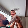 Magnus Grey joined the competition — help win amazing prizes! baby, man, beard, smiling, holding, window, indoor, ceiling_vent, tattoo, necklace, onesie, moon_pattern, hands, playful, father, parent, lift, happy, portrait, face