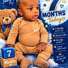 baby, infant, child, portrait, sitting, smiling, teddy_bear, milestone_photo, seven_months, blue_background, crown, stars, hearts, baby_clothing, orange_outfit, blanket, toys, wooden_blocks, name_block, indoor
