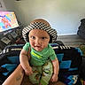 Bennett is registered to the contest to win money with this photo: baby, child, headphones, green_shirt, tattoos, lap, blanket, cartoon_tv, living_room, floor, person, tattooed_arm, foot, pants, patterned_pants, checkered, furniture, home_interior, portrait, cute