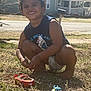 barefoot, casual_clothing, child, curly_hair, dirt, grass, happy, house, mailbox, nature, outdoor, play, road, smiling, squatting, suburban, summer, sunlight, toy_car, toy_truck