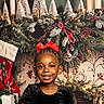 child, girl, smiling, red_bow, black_dress, christmas, holiday, decorations, candles, pine_branches, berries, gift, stocking, festive, indoors, portrait, happy, celebration, seasonal, background
