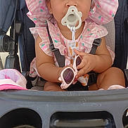 Madelaine is registered to the contest to win money with this photo: toddler, child, stroller, pacifier, sunglasses, pink_hat, pink_dress, baby, seatbelt, outdoor, face, cute, summer, accessory, infant, person, baby_clothes, happy, sitting, sun_hat