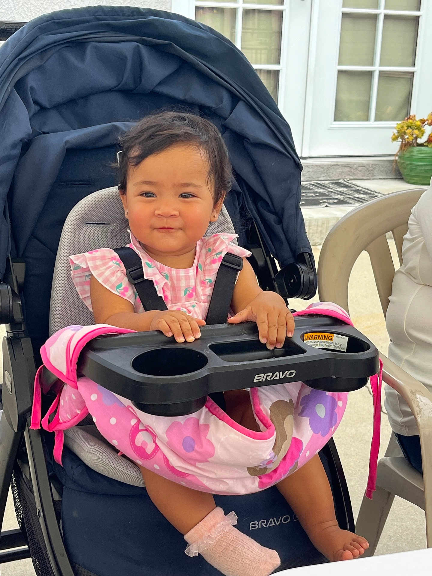 Madelaine is registered to the contest to win money with this photo: toddler, stroller, baby, pink_clothing, blanket, socks, outdoor, child, seat, baby_carrier, curly_hair, plastic_chair, door, smile, face, person, table, window, cushion, casual