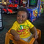 Lennox joined the competition — help win amazing prizes! baby, child, smiling, yellow_shirt, wooden_chair, arcade, game_machines, indoor, happy, cute, curly_hair, playful, seated, colorful, bright, fun, entertainment, person, young, joyful