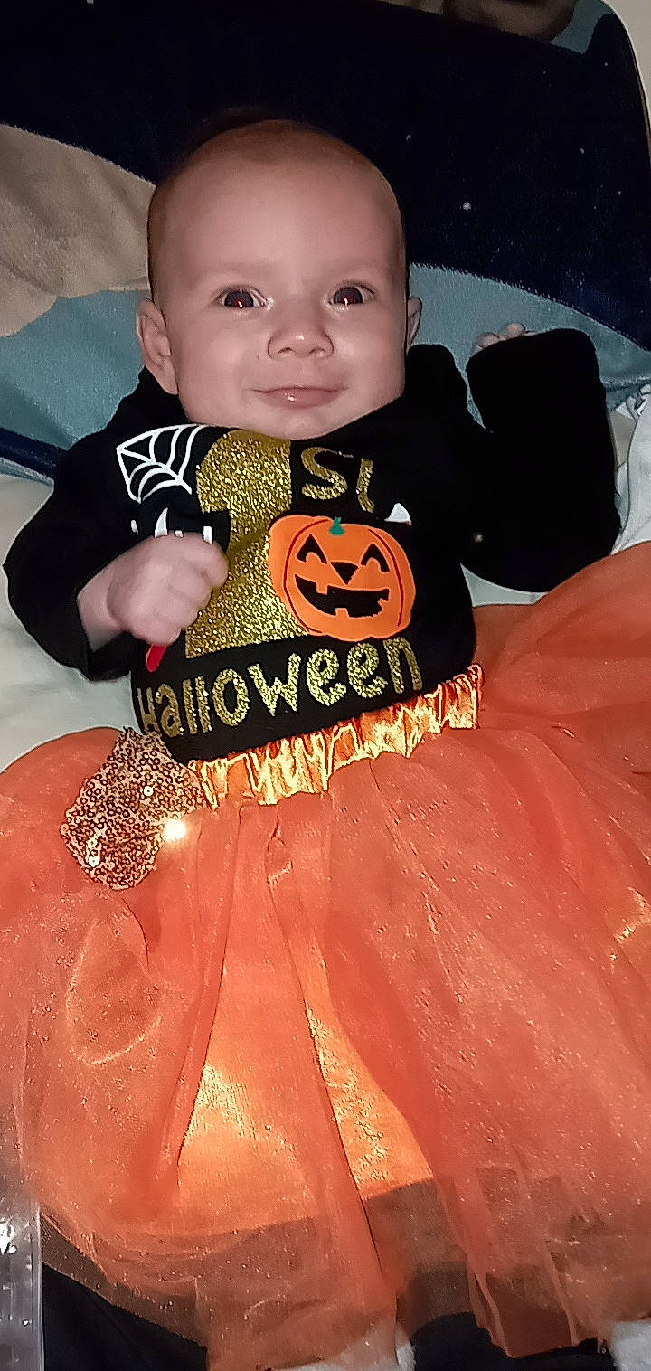 Annalise is registered to the contest to win money with this photo: baby, baby_products, baby_toddler_clothing, child, eye, face, flooring, fun, happy, head, joy, linens, orange, pattern, peach, person, sitting, skin, sleeve, t_shirt