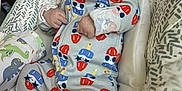 Maddox is registered to the contest to win money with this photo: baby, infant, pacifier, onesie, sleeper, baby_seat, cushion, patterned_clothing, indoor, cute, child, sleepwear, comfort, resting, young_child, colorful, soft_lighting, face, hands, footwear