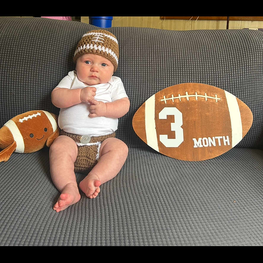 Maddox joined the competition — help win amazing prizes! 3_month, baby, child, couch, crochet, cute, football, gray_couch, hat, home_interior, infant, knitted_clothing, milestone, person, plush_toy, portrait, sitting, smiling_toy, white_shirt, wooden_sign