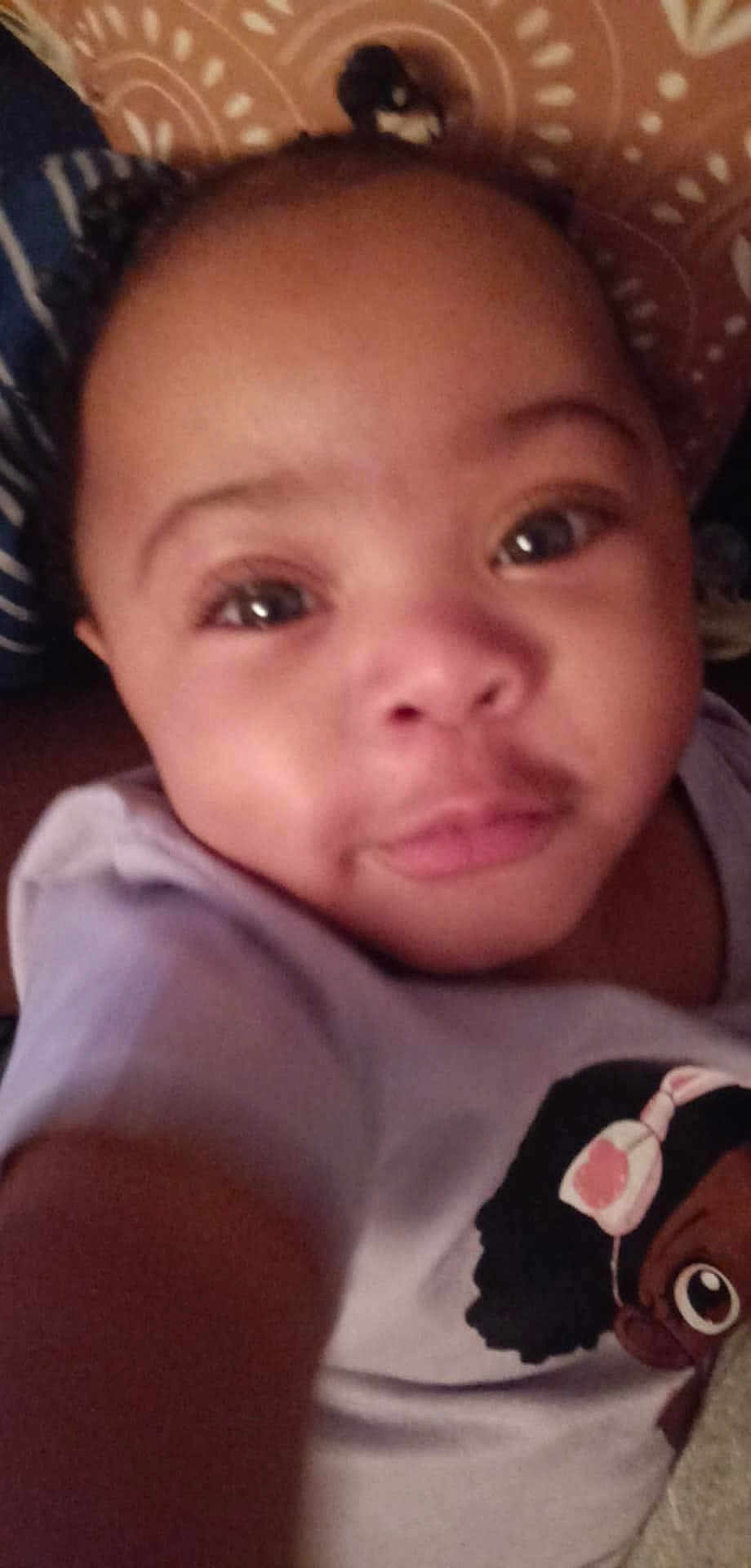 Daviana is registered to the contest to win money with this photo: baby, child, face, portrait, close_up, smile, eyes, skin, clothing, tshirt, cartoon, indoor, patterned_background, person, cute, infant, head, young_child, expression, selfie