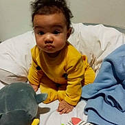 Kenza participe au concours pour gagner de l'argent avec cette photo : baby, child, yellow_outfit, curly_hair, bed, blanket, toy, stuffed_animal, sock, blue_blanket, indoor, person, infant, cute, expression, soft_toys, colorful, playtime, portrait, sitting