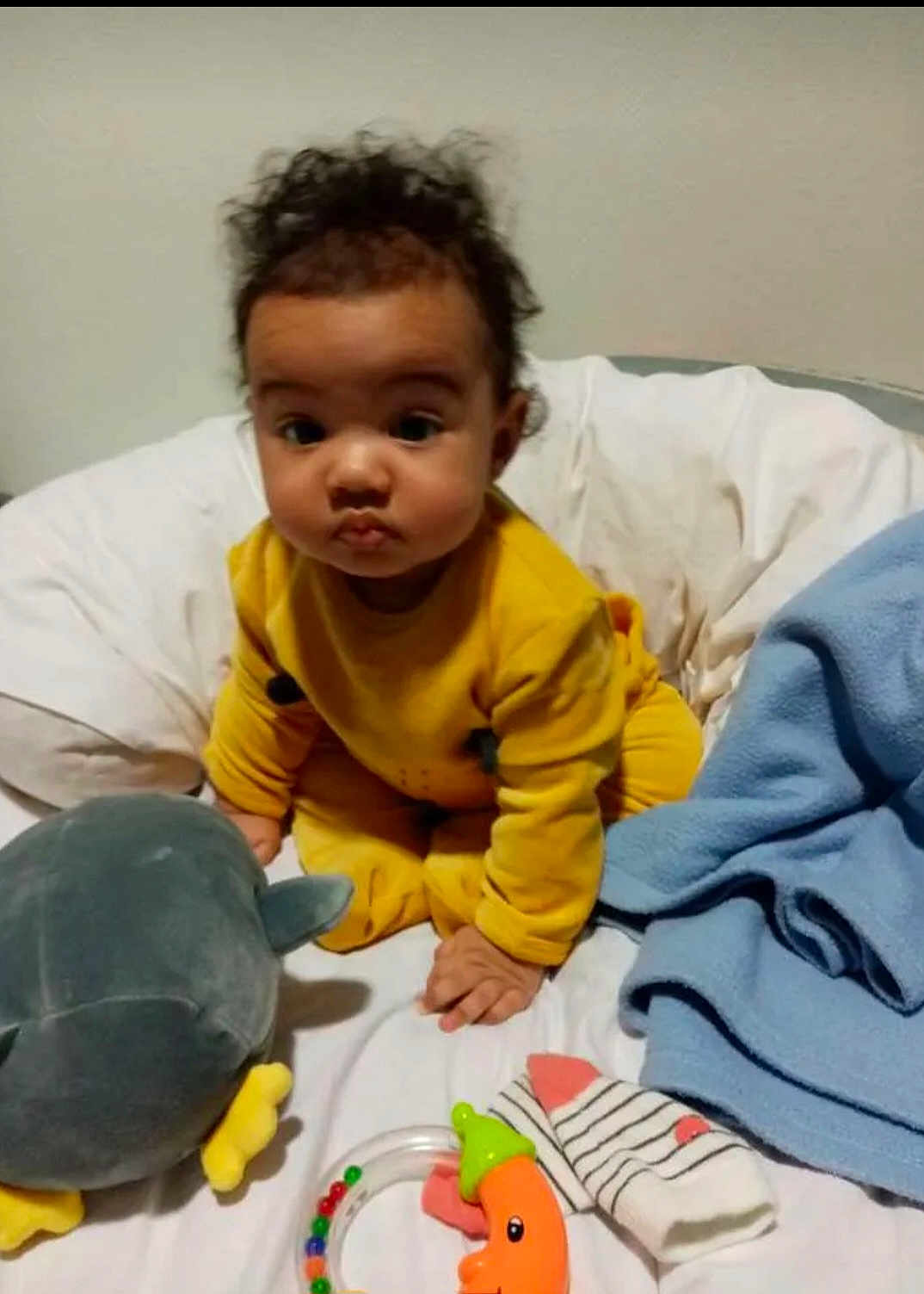 Kenza participe au concours pour gagner de l'argent avec cette photo : baby, child, yellow_outfit, curly_hair, bed, blanket, toy, stuffed_animal, sock, blue_blanket, indoor, person, infant, cute, expression, soft_toys, colorful, playtime, portrait, sitting