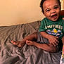 Kantrell joined the competition — help win amazing prizes! toddler, child, smiling, laughing, bed, comforter, green_shirt, shorts, indoor, person, happy, cute, young_child, sitting, barefoot, expression, joyful, skin, hair, furniture