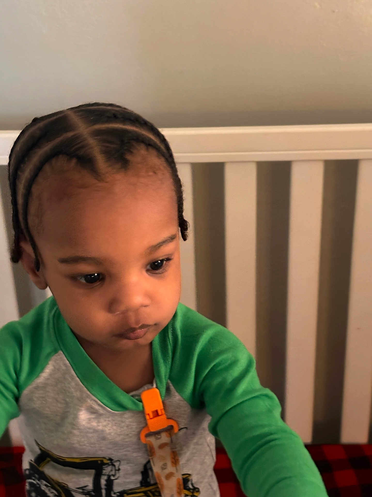 Kantrell is registered to the contest to win money with this photo: toddler, child, braided_hair, green_shirt, crib, indoor, young_child, calm, portrait, clothing, face, person, baby, infant, expression, sitting, home, cute, looking_down, furniture