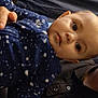 baby, child, infant, blue_fleece, patterned_clothing, hand, face, eyes, person, portrait, indoor, dark_background, clothing, reaching_hand, young_child, close_up, human, casual_wear, candid, baby_fashion