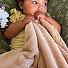 toddler, child, blanket, plush_toy, zebra, curly_hair, green_cushion, leaf_pattern, indoors, cozy, soft_texture, looking_away, yellow_clothing, earrings, cute, snuggled, comfort, baby, portrait, seated