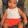 baby, child, car_seat, white_bow, headband, tank_top, orange_shorts, socks, infant, cute, wide_eyes, chubby_cheeks, seatbelt, indoors, portrait, person, clothing, sitting, young_child, casual