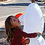 child, smiling, outdoor, inflatable, snowman, toy, playful, happy, casual_clothing, street, daylight, curly_hair, holiday_decoration, side_view, residential_area, stop_sign, car, pavement, fun, winter_theme