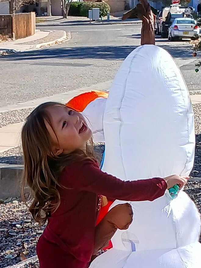 Aria joined the competition — help win amazing prizes! child, smiling, outdoor, inflatable, snowman, toy, playful, happy, casual_clothing, street, daylight, curly_hair, holiday_decoration, side_view, residential_area, stop_sign, car, pavement, fun, winter_theme