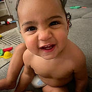 Jacob is registered to the contest to win money with this photo: toddler, child, smiling, face, indoor, couch, toy, carpet, bare_chest, cute, happy, person, home, living_room, playful, expression, sitting, close_up, curly_hair, diaper