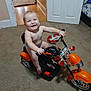Adriel is registered to the contest to win money with this photo: toddler, child, toy_motorcycle, indoor, carpet, bed, diaper, smiling, happy, play, furniture, room, floor, red_slide, handlebars, plastic_toy, head, face, person, baby