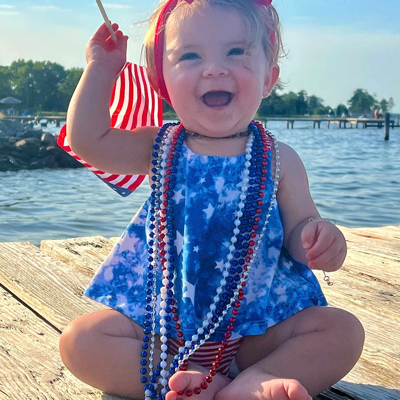 Everleigh is registered to the contest to win money with this photo: accessories, baby, clothing, dress, face, head, jewelry, lake, nature, necklace, person, photography, pier, port, portrait, summer, swimwear, water, waterfront, wood