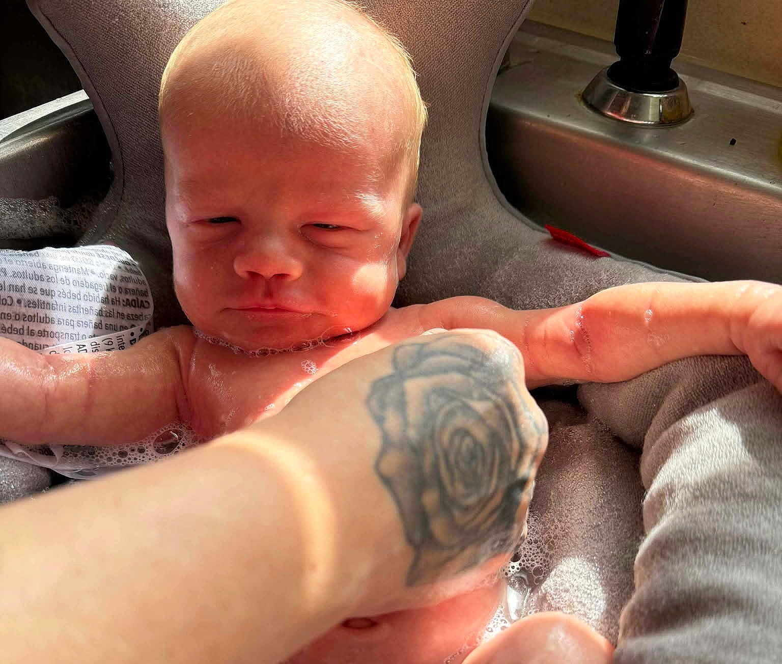 Simon is registered to the contest to win money with this photo: baby, infant, bath, water, bubbles, tattoo, hand, skin, face, expression, cushion, sink, light, shadow, arm, comfort, indoor, person, relaxation, parent