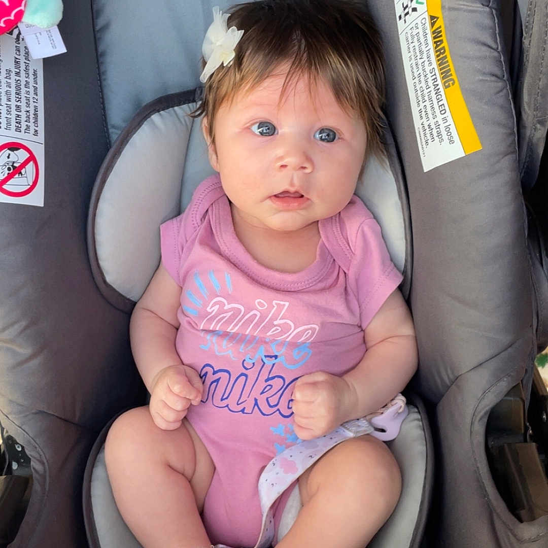 Satori Tewksbury joined the competition — help win amazing prizes! adorable, baby, baby_accessories, baby_girl, car_seat, car_seat_warning_label, child, child_safety, close_up, curious, cute, flower_hair_clip, indoor, infant, pink_onesie, portrait, seated, socks, soft_lighting, wide_eyes