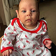 Lilibeth is registered to the contest to win money with this photo: baby, infant, clothing, onesie, red, white, hand, face, eyes, person, indoor, carpet, curtain, holding, cute, Liverpool_FC, newborn, portrait, expression, soft_light