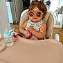 Ohana participe au concours pour gagner de l'argent avec cette photo : toddler, sunglasses, high_chair, baby_bottle, indoor, child, person, drink, table, curly_hair, bandana, pink_bow, plastic_container, wooden_floor, furniture, woman, blurred_background, casual_clothing, daylight, home