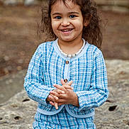Laya joined the competition — help win amazing prizes! child, smiling, girl, curly_hair, bow, pearl_necklace, blue_outfit, checkered, outdoor, rock, nature, portrait, happy, cute, fashion, sitting, young, person, casual, daylight