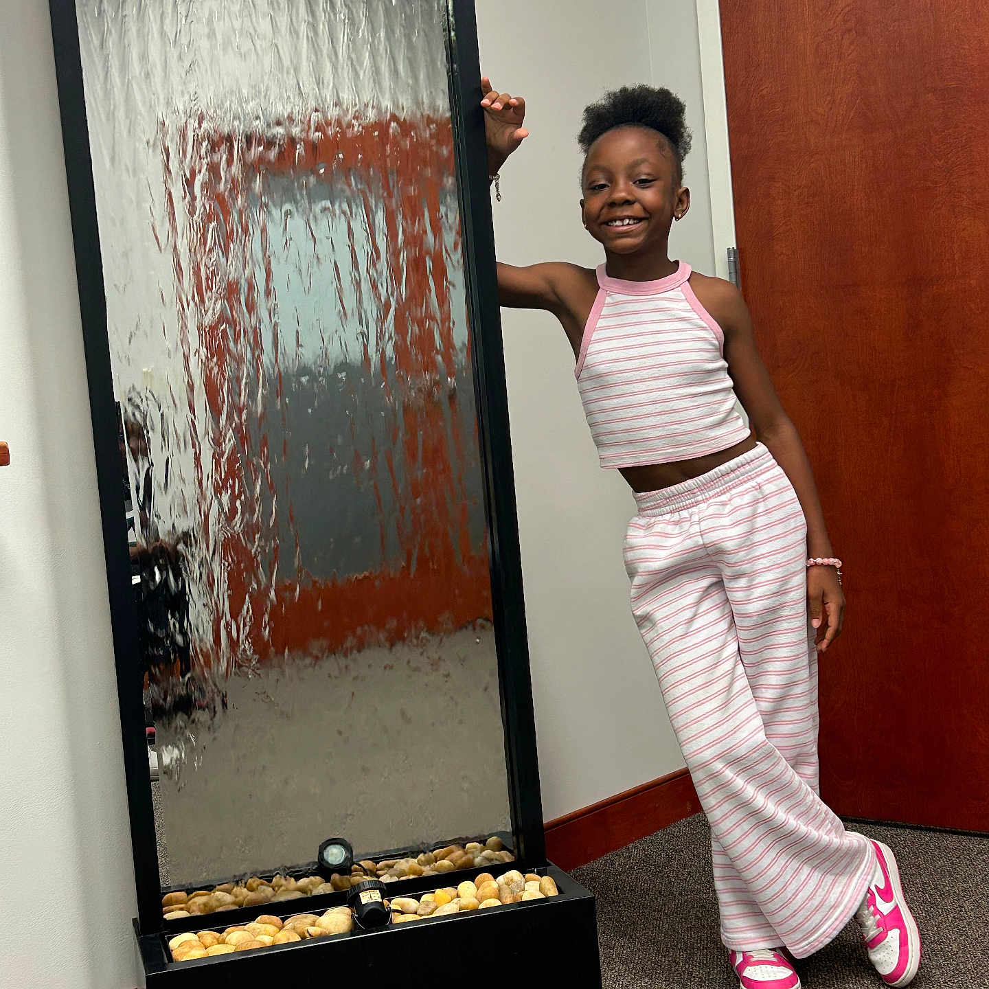 Avah joined the competition — help win amazing prizes! child, girl, smiling, striped_clothing, tank_top, pants, pink_shoes, sneakers, water_feature, indoor, carpet, door, wooden_door, standing, happy, bracelet, relaxed, casual, room, reflection