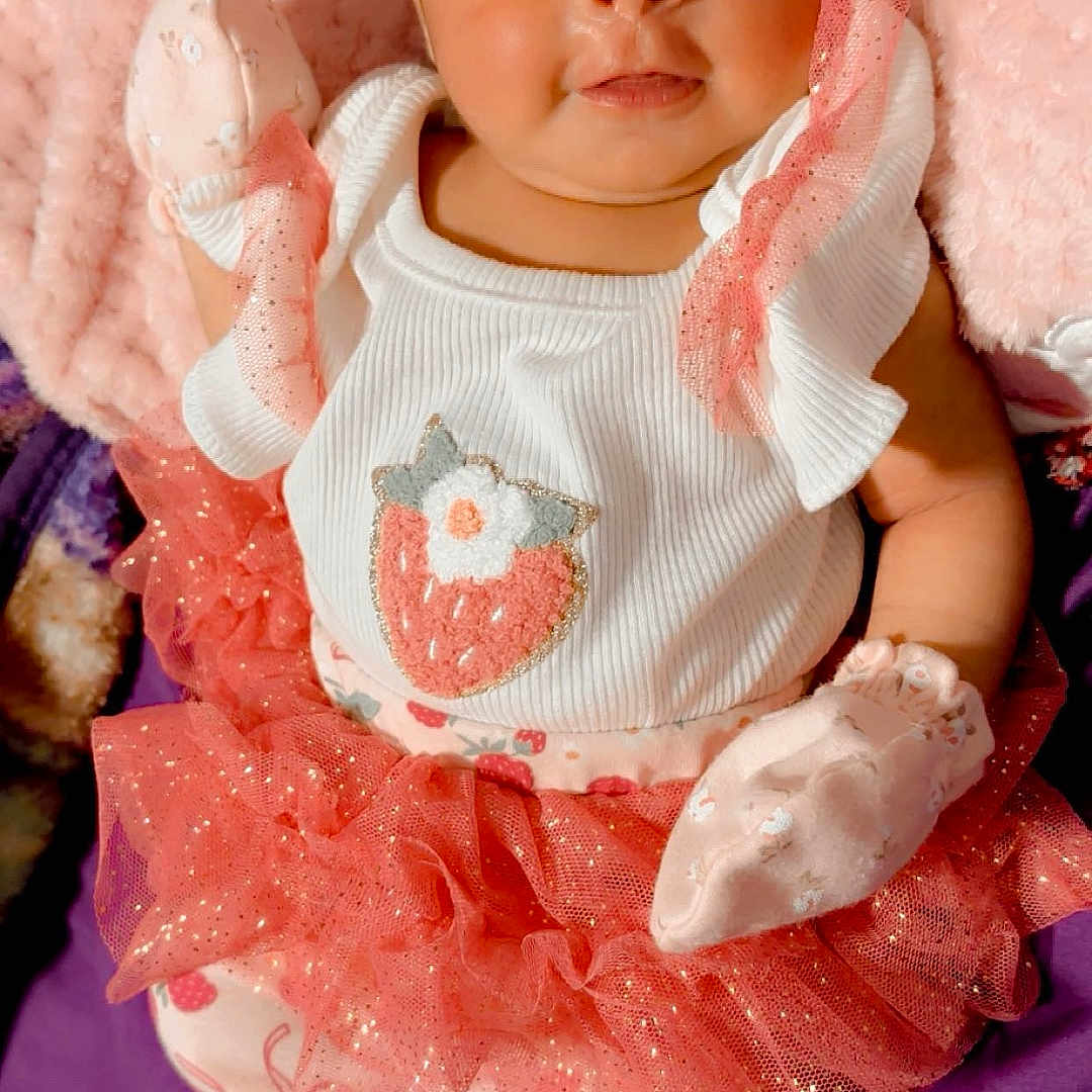 Areli is registered to the contest to win money with this photo: baby, blanket, bow, child, closeup, clothing, cute, dress, floral, headband, infant, lying_down, mittens, newborn, pink, plush, portrait, smiling, socks, tutu
