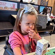 Tegan is registered to the contest to win money with this photo: brown_hair, casual, child, contemplative, dining, drink, fast_food, food, girl, high_chair, indoor, juice_box, menu, person, pink_sweatshirt, restaurant, seat, snack, table, white_bow