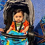 baby, stroller, blanket, child, orange_shirt, baby_shark, indoor, floor, hand, pink_shoe, carpet, seatbelt, person, cute, face, expression, clothing, footwear, toy_pattern, childcare