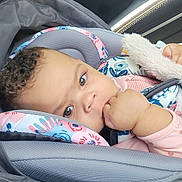 Avani joined the competition — help win amazing prizes! baby, child, car_seat, curly_hair, hand, thumb, blanket, car_interior, seatbelt, pink_clothing, face, infant, sitting, cute, closeup, person, young_child, safety, resting, car