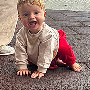 Julen joined the competition — help win amazing prizes! toddler, child, smiling, crawling, outdoor, beige_sweater, red_pants, happy, baby, footwear, shoe, person, face, blue_eyes, short_hair, pavement, texture, natural_light, casual_clothing, joyful