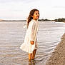 Neyla a rejoint le concours — aidez-le/la à gagner de superbes lots ! beach, child, cloudy, curly_hair, dress, girl, happy, nature, outdoor, playful, sand, shallow_water, shore, sky, standing, summer, water, waves, white_dress, young