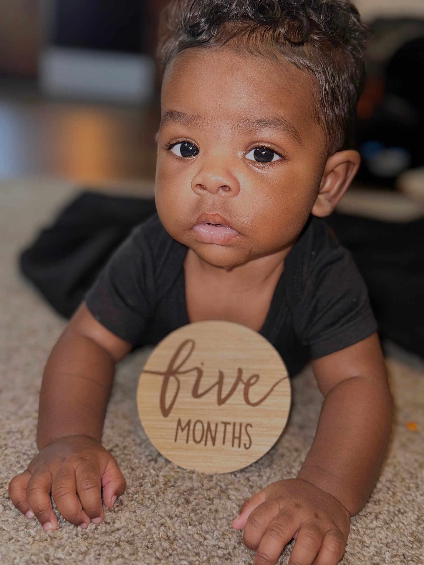 Gianni joined the competition — help win amazing prizes! baby, infant, five_months, carpet, wooden_sign, drool, black_shirt, curly_hair, close_up, face, hands, cute, indoors, child, portrait, young_baby, expression, skin, person, lying_down