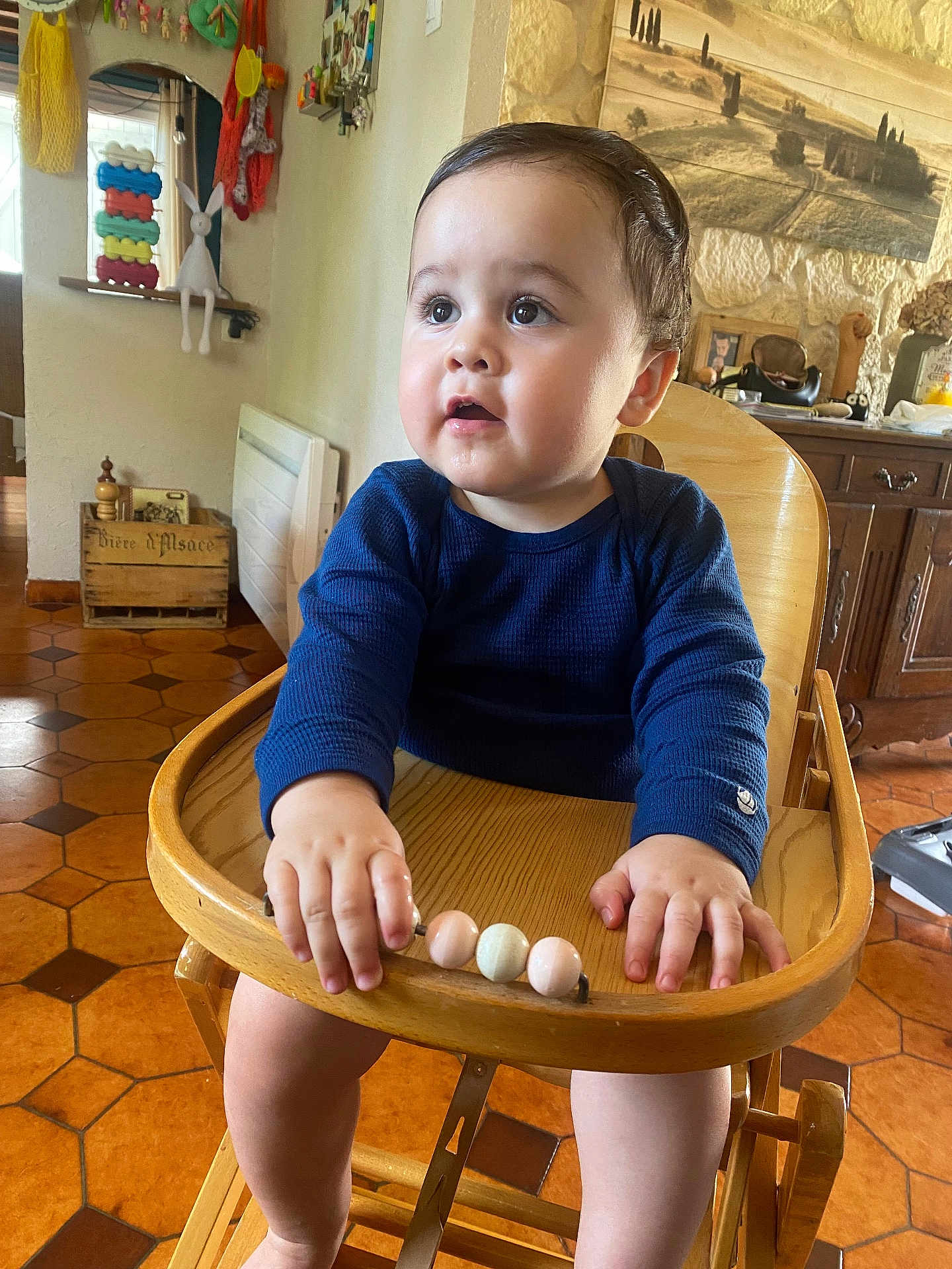 Marius a rejoint le concours — aidez-le/la à gagner de superbes lots ! baby, child, high_chair, wooden_furniture, indoor, toy_beads, curious, navy_shirt, hands, face, legs, kitchen, floor_tiles, decor, window, light, person, cute, infant, home