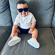 Israel joined the competition — help win amazing prizes! baby, child, sunglasses, white_tshirt, white_sneakers, smiling, couch, indoor, cute, fashion, young_child, sitting, casual, funny, portrait, person, footwear, accessory, happy, plush