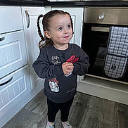 Rain is registered to the contest to win money with this photo: child, girl, braids, pigtails, sweatshirt, cartoon, kitchen, floor, oven, cabinet, socks, curious, standing, indoors, appliance, countertop, home, smile, cute, portrait