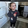 child, girl, braids, pigtails, sweatshirt, cartoon, kitchen, floor, oven, cabinet, socks, curious, standing, indoors, appliance, countertop, home, smile, cute, portrait
