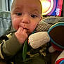 baby, child, camouflage, pajamas, teething, fingers, soft_toy, toy, living_room, television, blurred_background, closeup, face, person, indoor, cute, young_child, hand, couch, curious