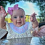 baby, child, girl, pink_bow, bib, smiling, happy, portrait, closeup, hands, outdoor, daylight, face, cute, infant, clothing, table, background_blur, headband, person