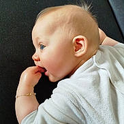 Elya participe au concours pour gagner de l'argent avec cette photo : baby, infant, child, blue_eyes, white_clothing, bracelet, fingers_in_mouth, lying_down, curious_expression, hair_tuft, indoor, soft_light, close_up, portrait, cute, skin, face, hand, baby_gesture, cozy