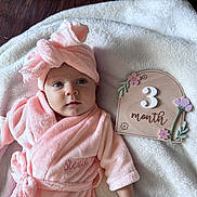 Stevie is registered to the contest to win money with this photo: baby, baby_sign, blanket, child, eyes, face, flowers, fluffy, indoor, infant, lying_down, milestone, photography, pink, portrait, robe, smiling, three_months, towel, wood_floor